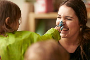 A child touching the nose of an Educator with paint on their hand